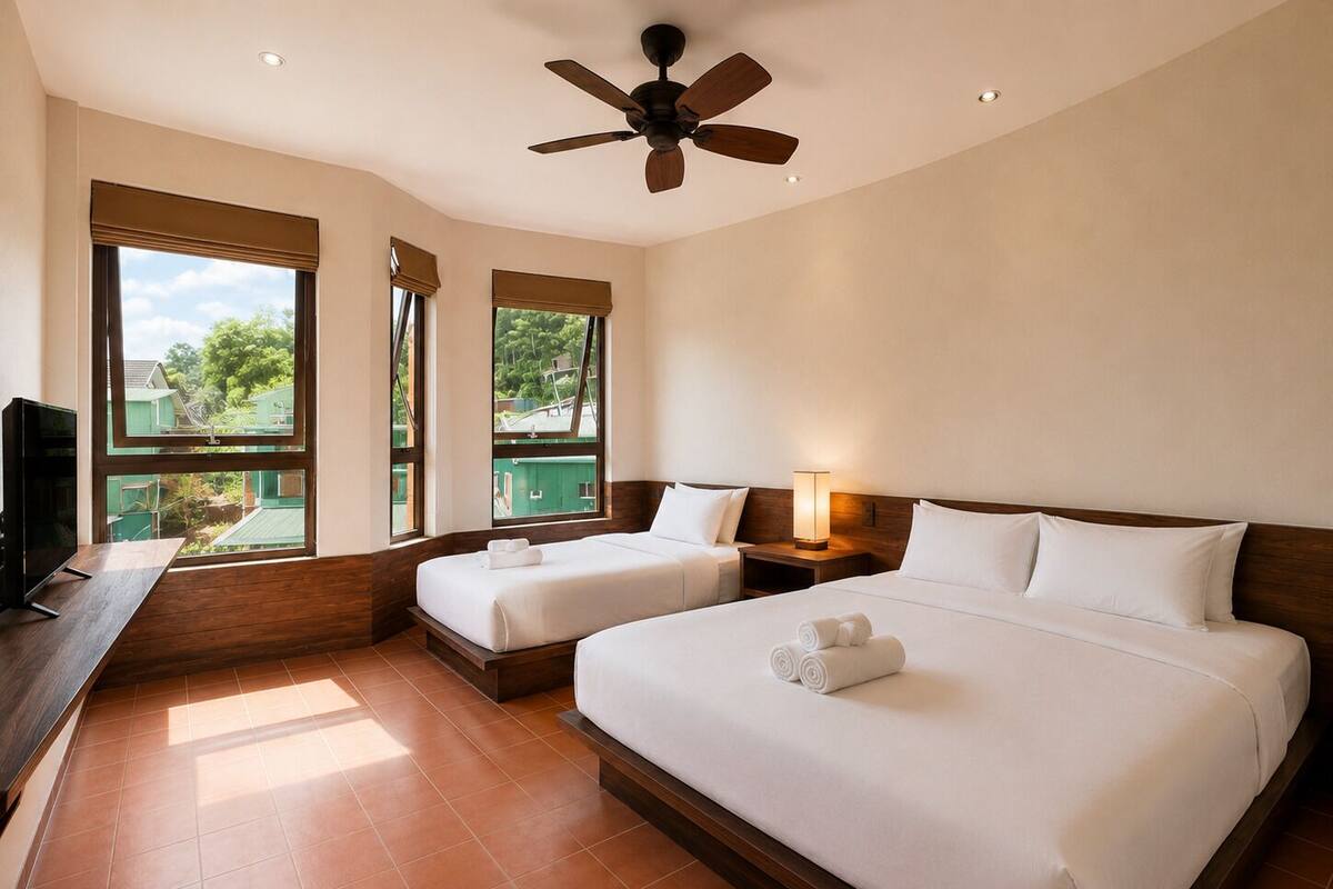 A hotel room with two beds, a TV, a ceiling fan, and large windows with a view of greenery.