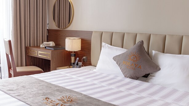 A hotel room with a bed, a desk with a telephone, a lamp, a mirror, and a pillow with text. - Solaya hotel (Van Don)