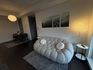 A modern living room with a unique, textured sofa, a dining area with a small table and chairs, and a large floor lamp.