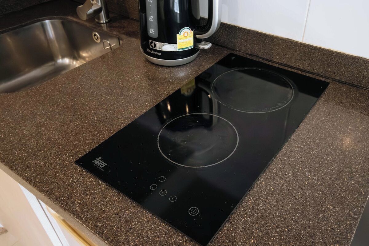 A kitchen with a black induction cooktop, a stainless steel sink, and a coffee maker.