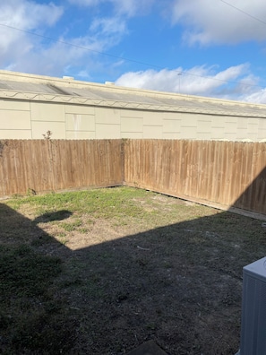 A fenced backyard with a grassy area and a building with a flat roof.