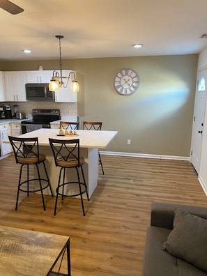 A modern kitchen with a central island, bar stools, a clock, and a dining area.