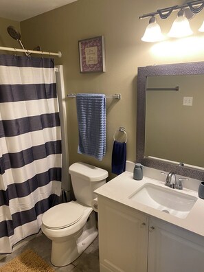 Ein Badezimmer mit gestreifter Duschvorhang, Toilette, Waschbecken mit Spiegel und Handtuchhalter.