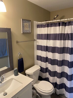 A bathroom with a white sink, a toilet, a shower curtain, a towel rack, and a framed quote on the wall.