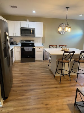 A kitchen with white cabinets, a microwave, a stove, and a dining area with a table and chairs.