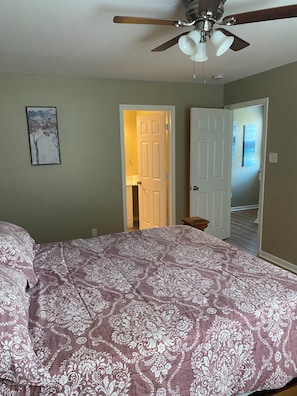 A bedroom with a bed, a ceiling fan, and a door leading to another room.