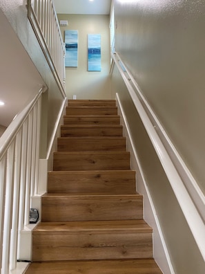A wooden staircase with white railings and a handrail, leading to a landing with two framed artworks on the wall.