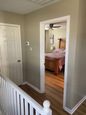 Ein Flur, der zu einem Schlafzimmer mit einem Bett, einem Deckenventilator und einer Holzkommode führt.