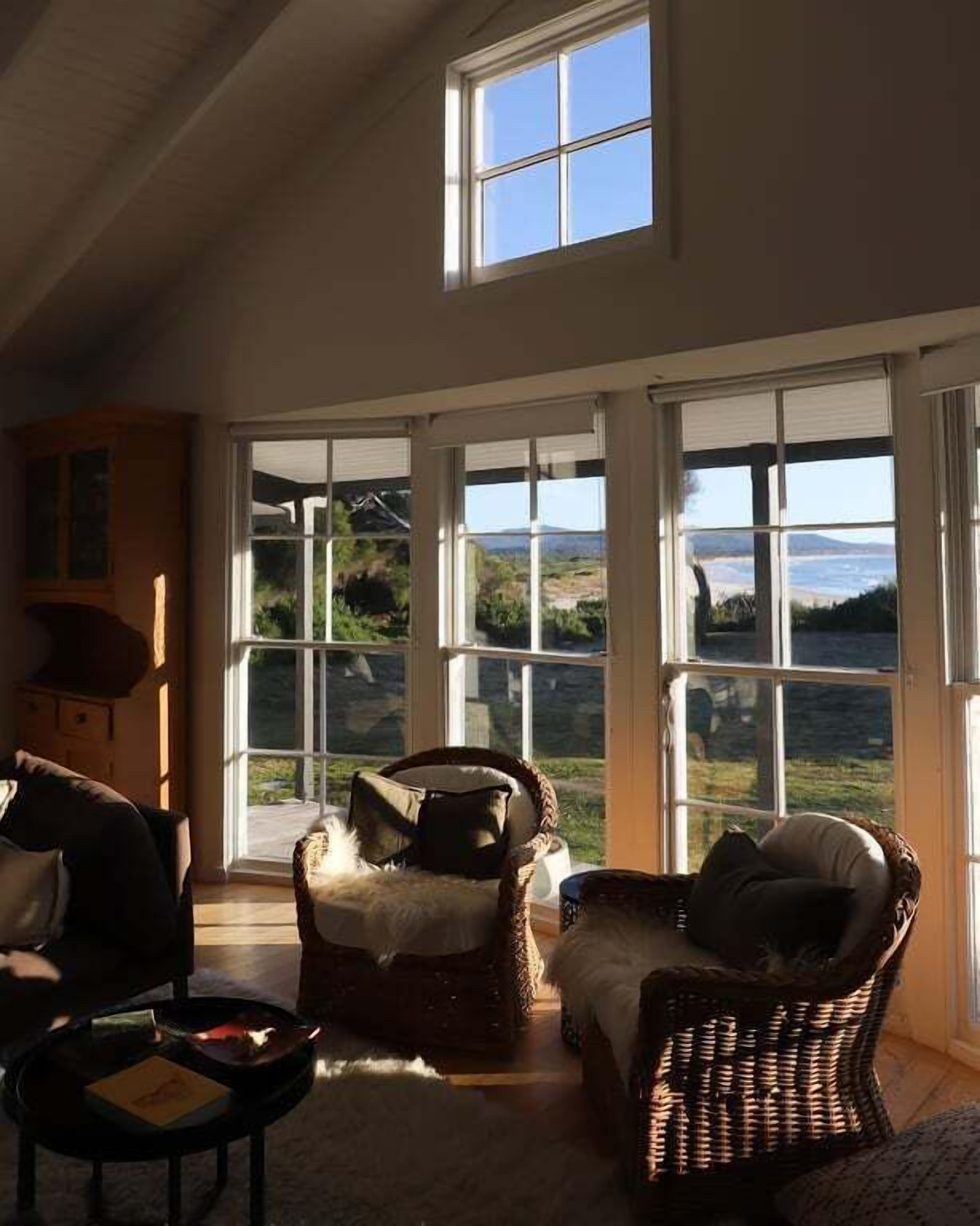 Ein Zimmer mit großen Fenstern, Korbmöbeln und Blick auf eine Landschaft.