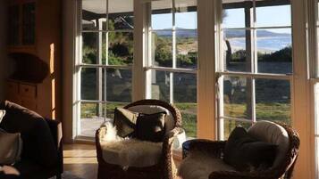 Ein Zimmer mit großen Fenstern, Korbmöbeln und Blick auf eine Landschaft.