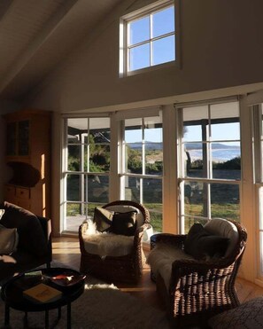 Ein Zimmer mit großen Fenstern, Korbmöbeln und Blick auf eine Landschaft.