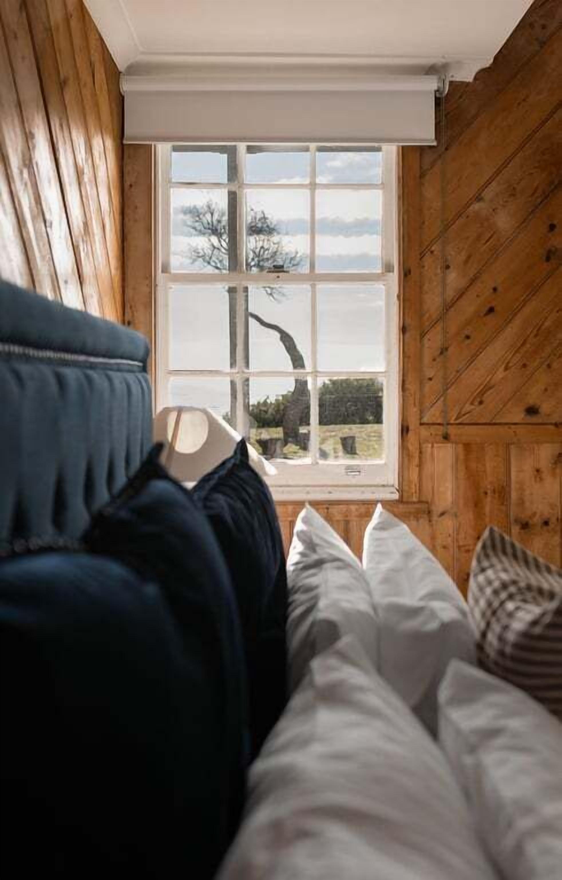 A bedroom with a large window, wooden walls, and a bed with white and dark bedding.
