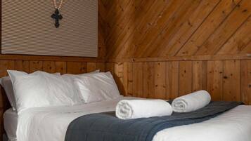 A wooden-paneled room with a bed, white bedding, and a cross pendant on the wall.