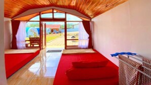 Um quarto com teto inclinado, um sofá vermelho, uma mesa pequena e vista através de uma janela grande.
