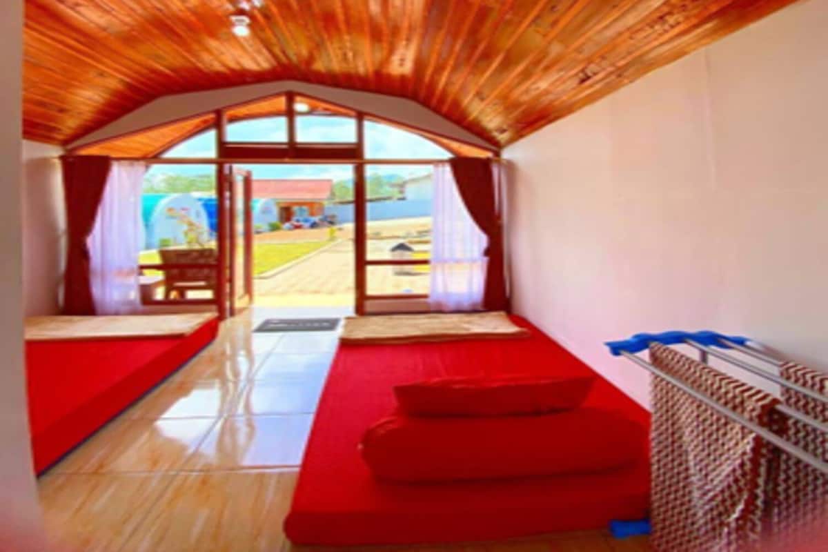 Ein Zimmer mit schrägen Wänden, einem roten Sofa, einem kleinen Tisch und Blick durch ein großes Fenster.