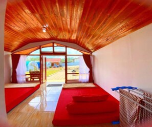 A room with a sloped ceiling, a red sofa, a small table, and a view through a large window. - Cozzy Rompok Cileunca (bandung)