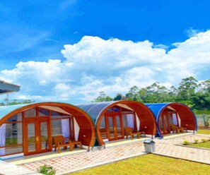A row of circular wooden cabins with glass doors and windows, a paved walkway, and a grassy area. - Cozzy Rompok Cileunca (bandung)