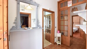 Un passadís amb una porta de fusta, un mirall, una taula petita amb un recipient rosa i un sòl de rajola.