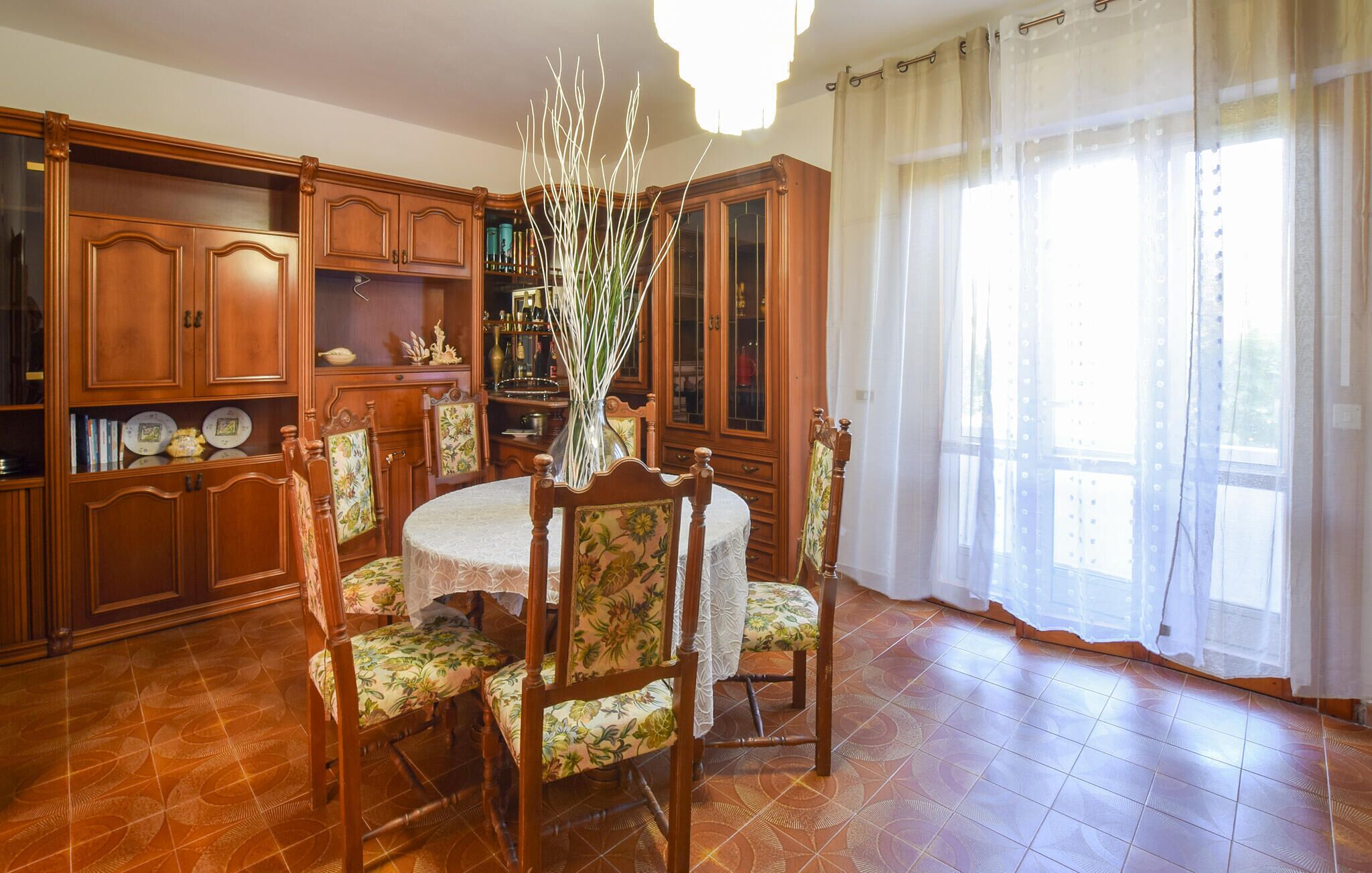 Una sala da pranzo con un tavolo rotondo, sedie floreali, mobili a parete in legno e un'ampia finestra con tende leggere.