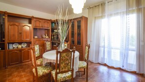 Una sala menjador amb una taula rodona, cadires florals, armaris de fusta i un gran finestral amb cortines lleugeres.