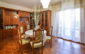 A dining room with a round table, floral chairs, wooden cabinets, and a large window with sheer curtains. - 2 bedroom nice apartment in Rosignano Solvay (Rosignano Solvay)