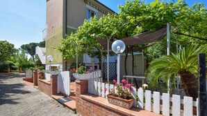 Un edifici amb una zona d'estar exterior coberta, una tanca de palets blancs i plantes en testos.