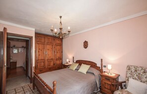 Ein Schlafzimmer mit einem hölzernen Bett, einer Pendelleuchte, einem Nachttisch und einem Sessel.
