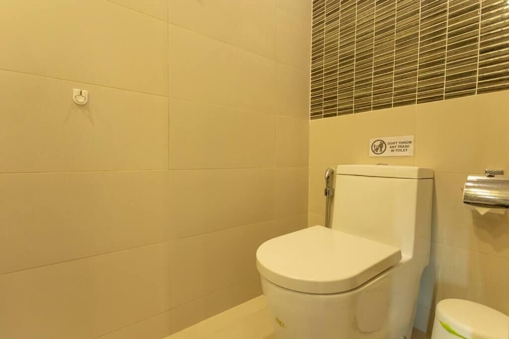 A small, clean bathroom with a toilet, a hand dryer, and a sign instructing not to throw trash in the toilet.