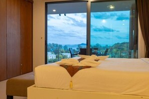 A bedroom with a large window, a bed, a wooden wardrobe, and a view of the cityscape. - Sea View the tree 1BR Condo 500m Walk 2 BeachC260 (Tambon Rawai)