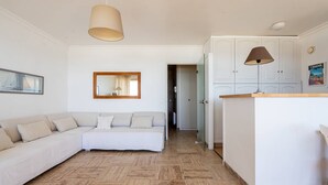 Ein modernes Wohnzimmer mit einer Couch, einem Spiegel, einer Pendelleuchte und einer Küchenzeile mit Schränken und einer Arbeitsplatte.