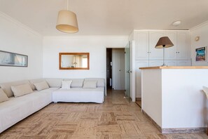Een moderne woonkamer met een bank, een spiegel, een hanglamp en een keuken met kasten en een aanrecht.