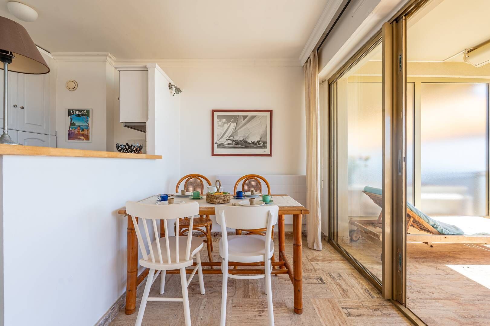Un coin repas avec une table dressée pour quatre personnes, un tableau encadré au mur et une porte-fenêtre coulissante donnant sur un balcon.