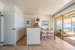 Een compacte keuken met een eethoek, een klein kookeiland, en uitzicht door een schuifdeur op een balkon.