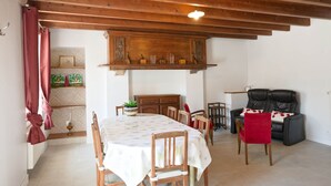 A dining area with a table set for four, wooden chairs, a red chair, a sofa, and a wooden ceiling with exposed beams.