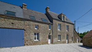 A stone building with a blue garage door, a small stone structure with a gate, and a clear sky.