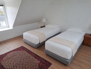 A room with two beds, a nightstand with a lamp, a patterned rug, and a window with a view. - Louise's House (Varouville)