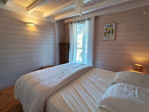 Ein Schlafzimmer mit einem Bett, Holzwänden, einem Fenster mit Vorhängen und einer Wandlampe.