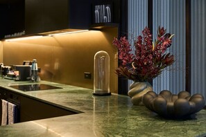 A modern kitchen with a built-in stove, a glass-enclosed coffee machine, and a decorative vase with flowers. - The Grand Heritage Suite · 4 Bed · Entire Floor (Auckland City)