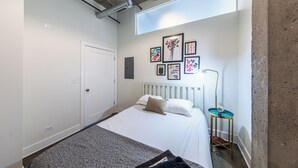 A bedroom with a bed, a wall-mounted artwork, a bedside table, and a window.