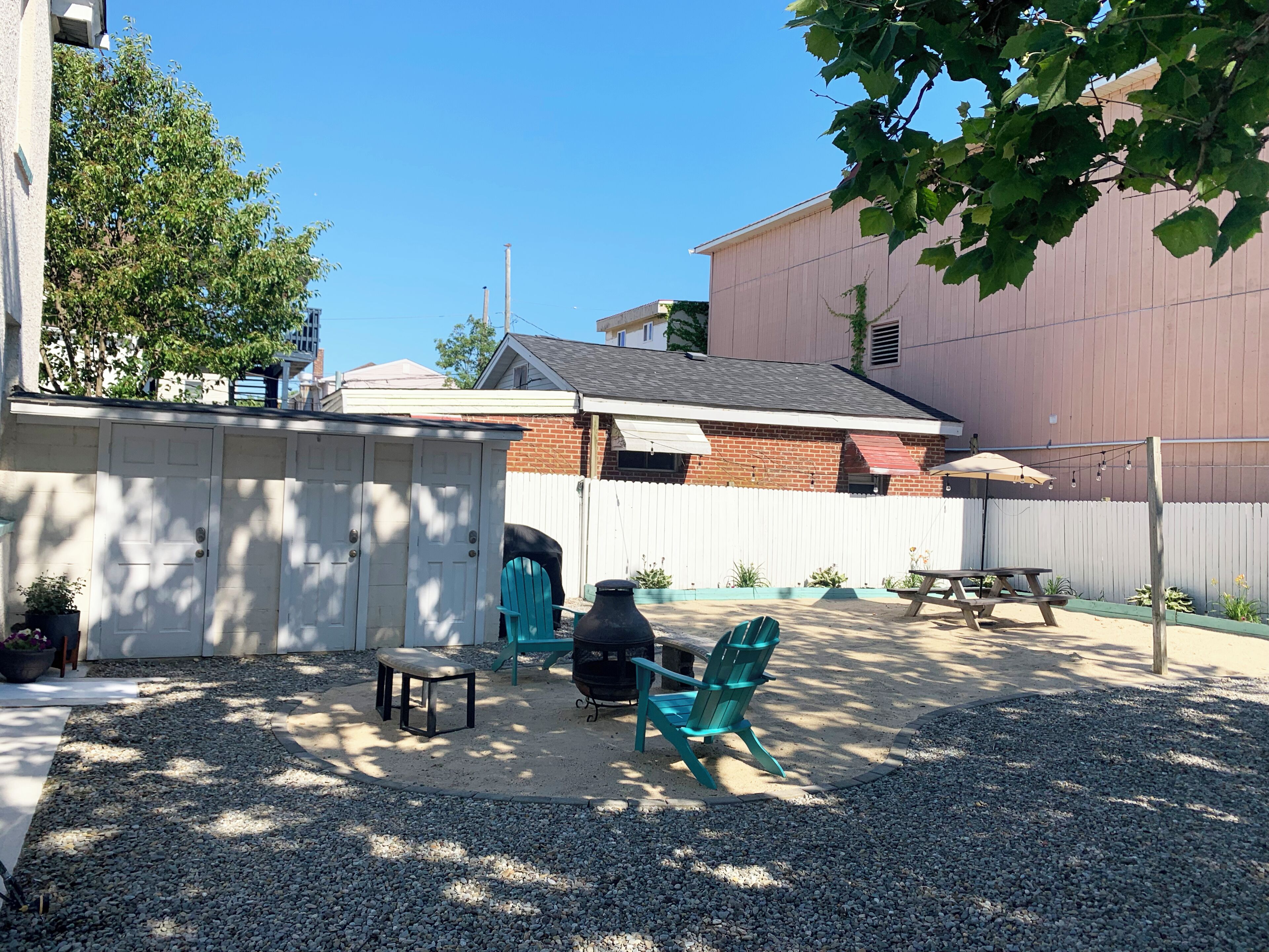 A backyard with a barbecue grill, outdoor seating, and a white fence.