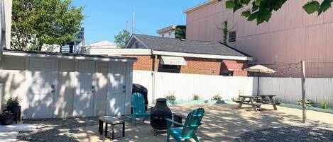A backyard with a barbecue grill, outdoor seating, and a white fence.