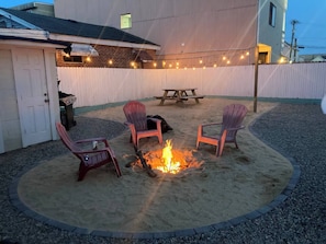 Ein Garten mit Feuerschale, vier Adirondack-Stühlen, einem Picknicktisch und Lichterketten.