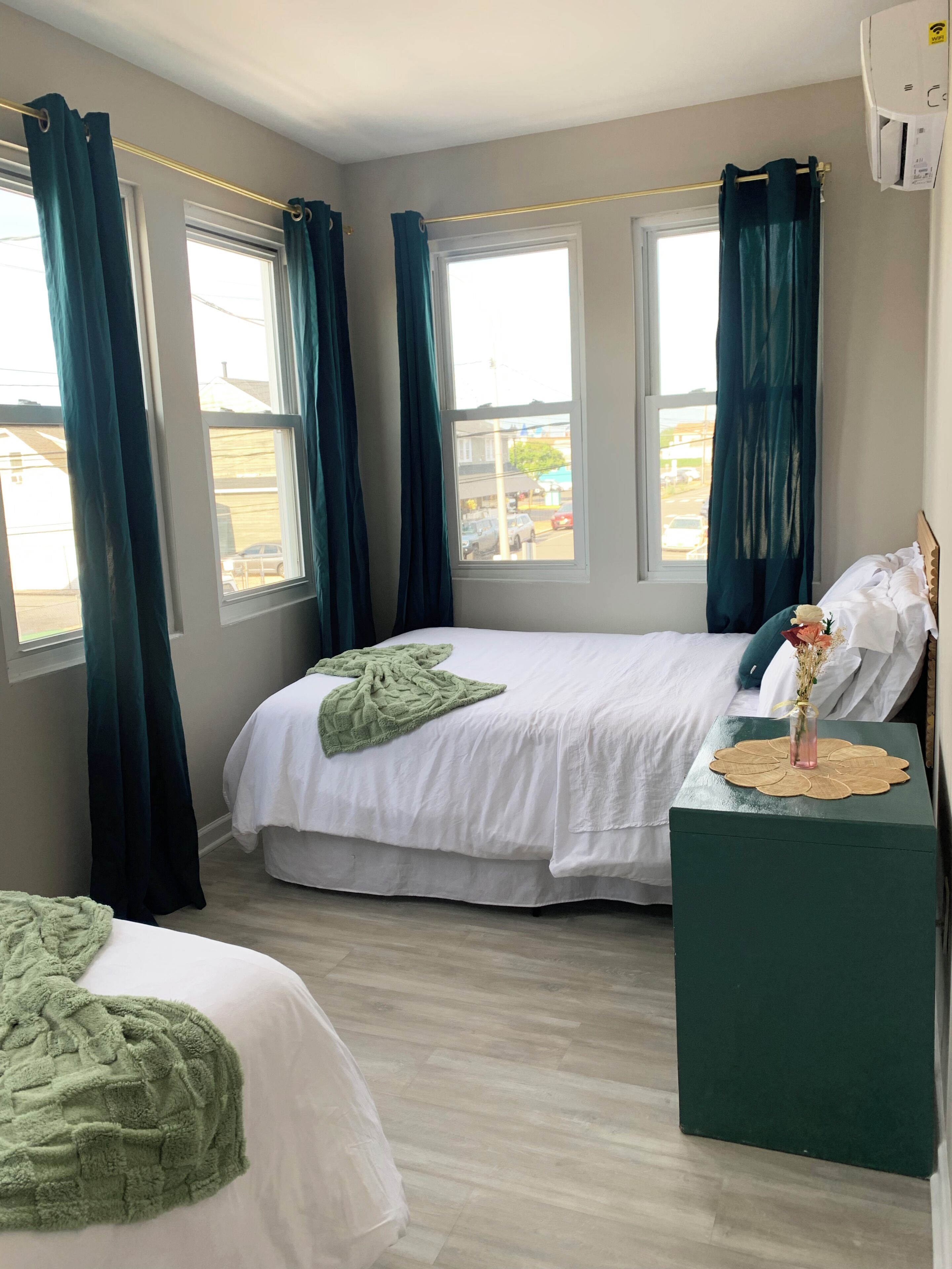 Un dormitorio con dos camas, una ventana, una mesita de noche con un florero y una mesita de noche verde.