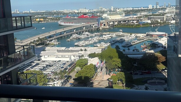 Un edificio de gran altura con varios balcones que dan a una marina con barcos y un paisaje urbano al fondo.