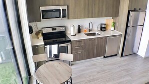 Una cocina moderna con microondas, estufa, lavaplatos y refrigerador. Hay un comedor con mesa y sillas.