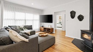 Una sala de estar moderna con un sofá modular, un televisor de pantalla plana, una chimenea y piso de madera.