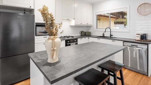 Una cocina moderna con armarios blancos, un refrigerador de acero inoxidable, una isla central con taburetes y un ventanal con vistas.