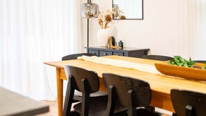 Un comedor con mesa de madera, sillas negras, un florero con flores secas y un espejo en la pared.