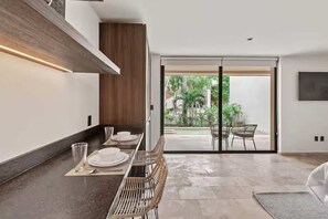A modern dining area with a long table, chairs, and a view through glass doors to an outdoor space.