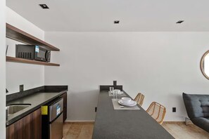 Une cuisine moderne dotée d’appareils électroménagers intégrés, un coin repas avec une longue table et un canapé.
